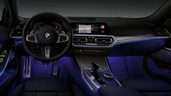 BMW 3-serie Sedan (G20), Ambient Light. Cockpittet i førersiden i BMW 3-serie Sedan (G20) set forfra med fodbrønd med blåt Ambient Light.