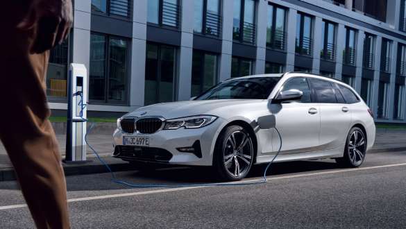 Plug-in-hybrid BMW 3er Touring 2021 G21 set forfra under ladning Plug-in-hybrid BMW 3-serie Touring 2021 G21 forfra let drejet under ladning foran en bygning