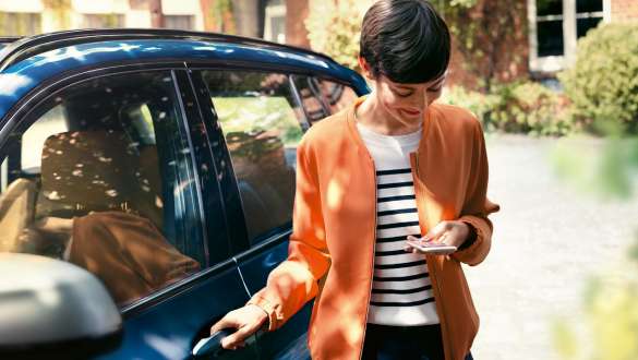 En kvinde kigger på sin smartphone og åbner døren til sin BMW BMW Teleservices en kvinde kigger på sin smartphone og åbner døren til sin BMW