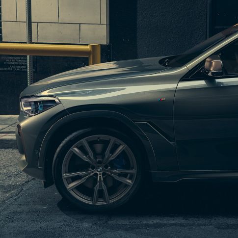 BMW X6 M50i set fra siden En mand læner sig op ad BMW X6 M50i set fra siden foran et urbant miljø