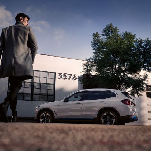 BMW iX3 G08 set fra siden med en mand foran en bygning BMW iX3 G08 2020 Mineral White metallic set fra siden med en mand foran en bygning