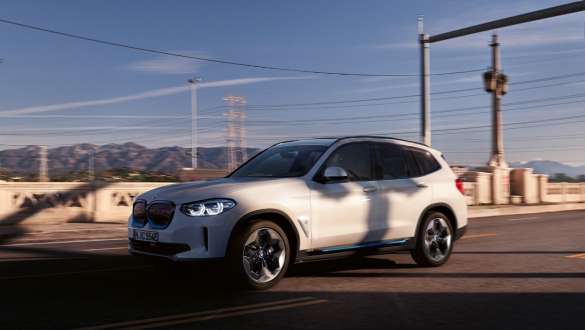 Adaptiv M undervogn BMW iX3 G08 kørende på en vej Adaptiv M undervogn BMW iX3 G08 2020 Mineral White metallic set forfra let drejet kørende på en vej