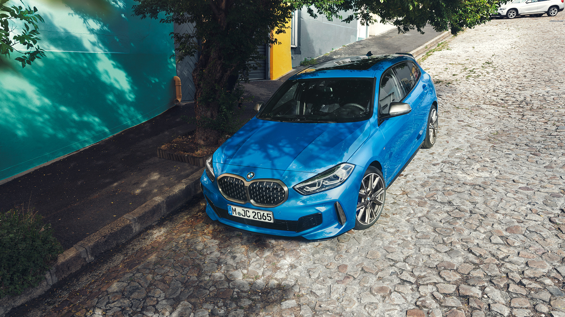 1-Serie BMW i vejkanten. 1-serie BMW i Misano Blue metallic set forfra let drejet i vejkanten fra fugleperspektiv, mens den parkerer.