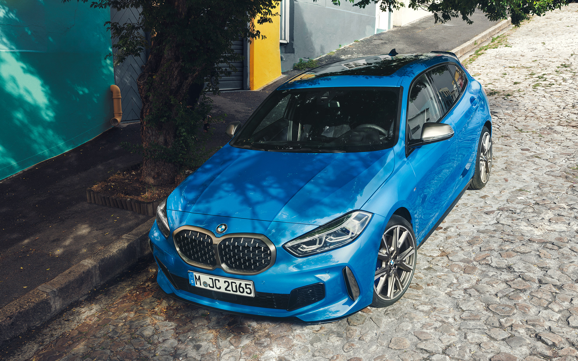 BMW 1-serie M135i F40 i vejkanten BMW 1-serie M135i F40 i Misano Blue metallic, set forfra let drejet i vejkanten fra fugleperspektiv under parkering