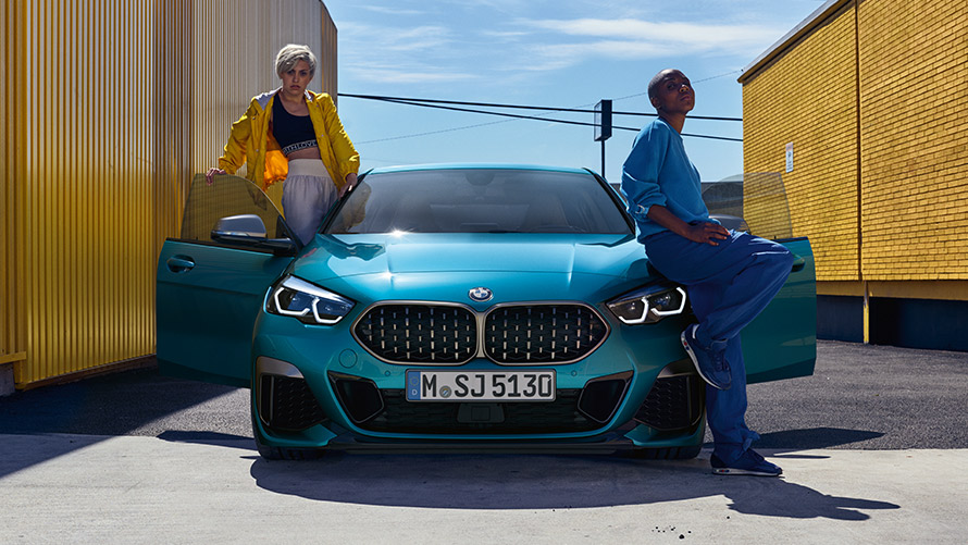 BMW 2-serie Gran Coupé F44, set forfra BMW 2-serie Gran Coupé F44 Snapper Rocks Blue metallic, set forfra med åbne døre og to personer ved bilen