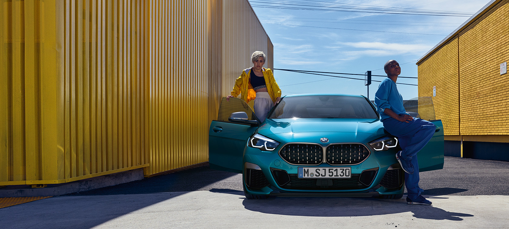 BMW 2-serie Gran Coupé F44, set forfra BMW 2-serie Gran Coupé F44 Snapper Rocks Blue metallic, set forfra med åbne døre og to personer ved bilen