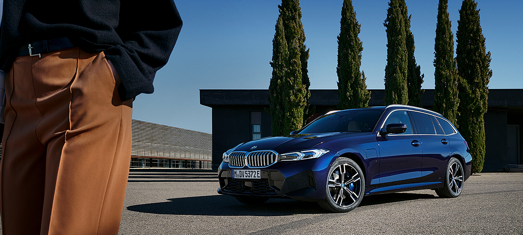 BMW 3-serie Touring LCI G21 Tanzanite Blue II set forfra let drejet stående foran træer