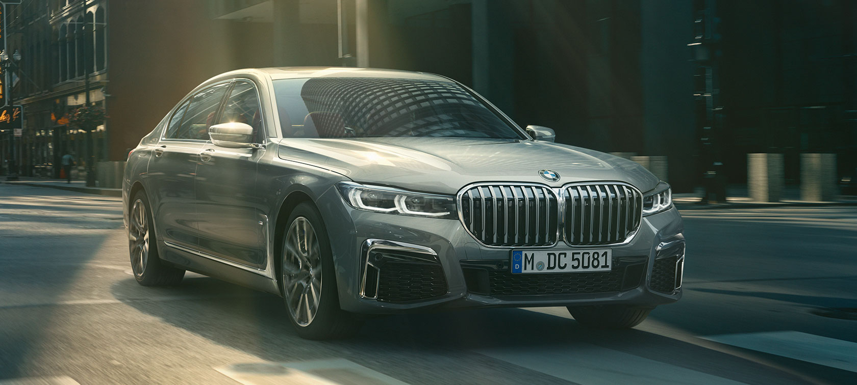 Grå BMW 7-serie Sedan kørende, set forfra let drejet Grå BMW 7-serie Sedan kører i urbant miljø set forfra let drejet