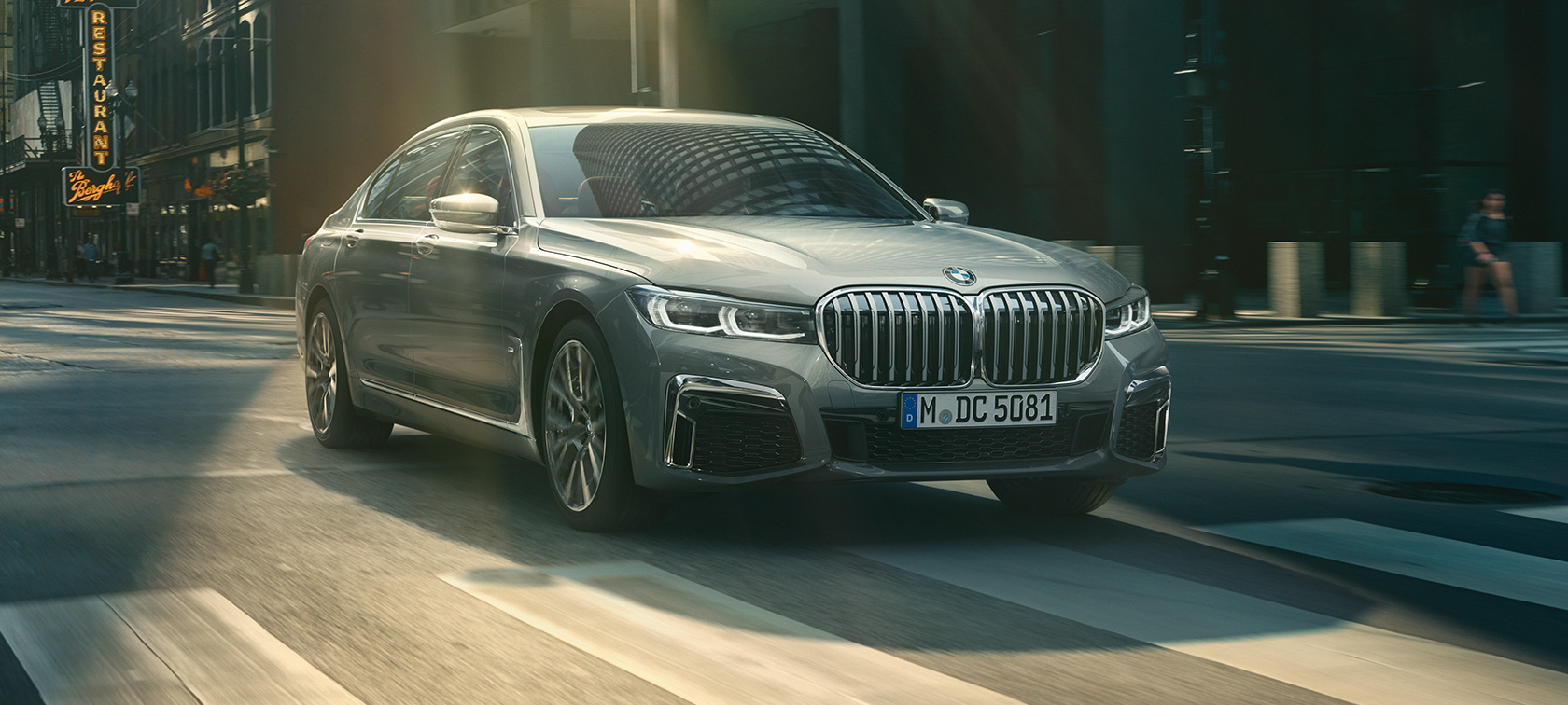 En grå BMW 7-serie Sedan kørende, set forfra let drejet En grå BMW 7-serie Sedan kører i urbant miljø set forfra let drejet