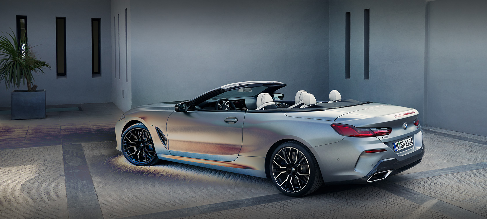 Mand læner sig op ad BMW 8-serie Cabriolet G14 LCI Facelift 2022 BMW Individual BMW Individual Frozen Pure Grey metallic set fra siden stående foran en bygning