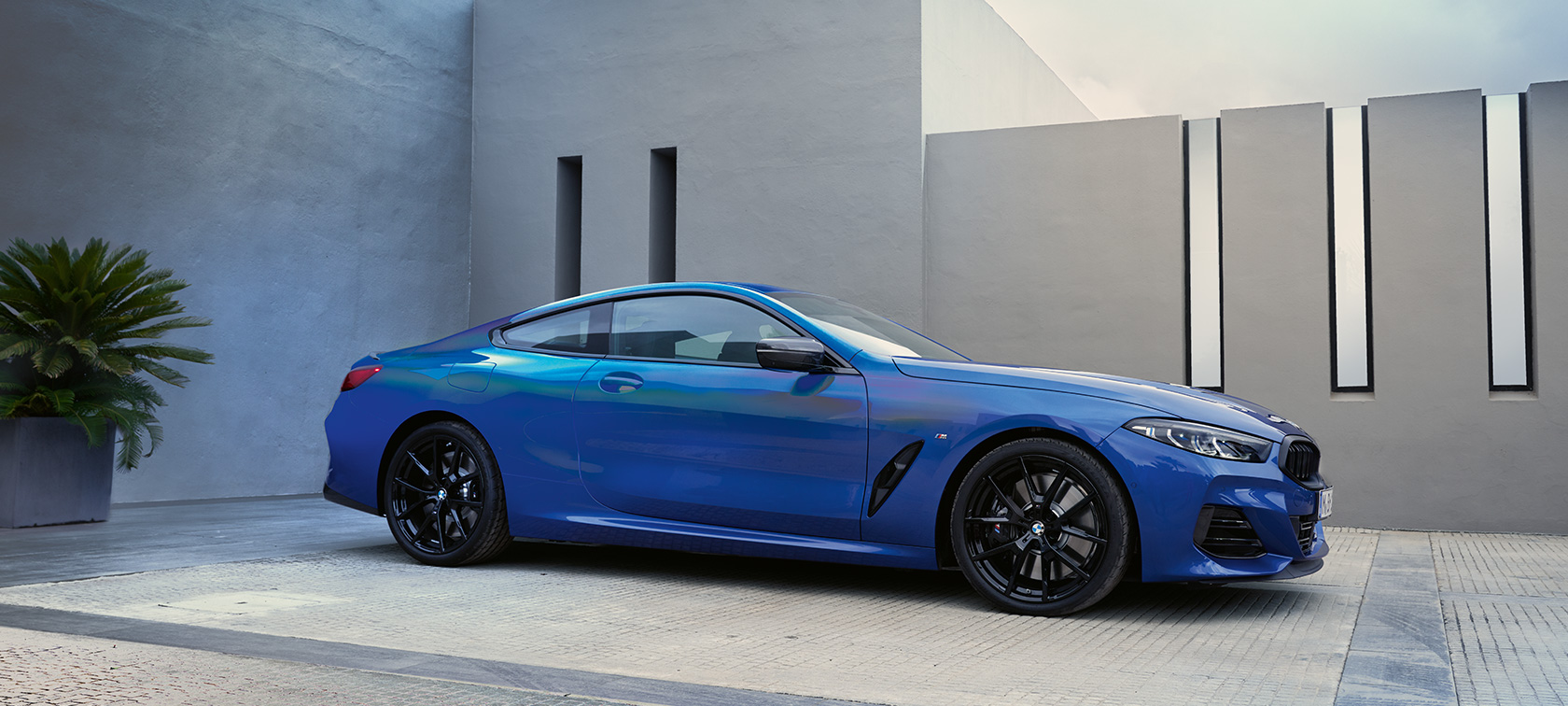 BMW 8-serie Coupé G15 LCI Facelift 2022 M Portimao Blue metallic set fra siden stående foran husmur