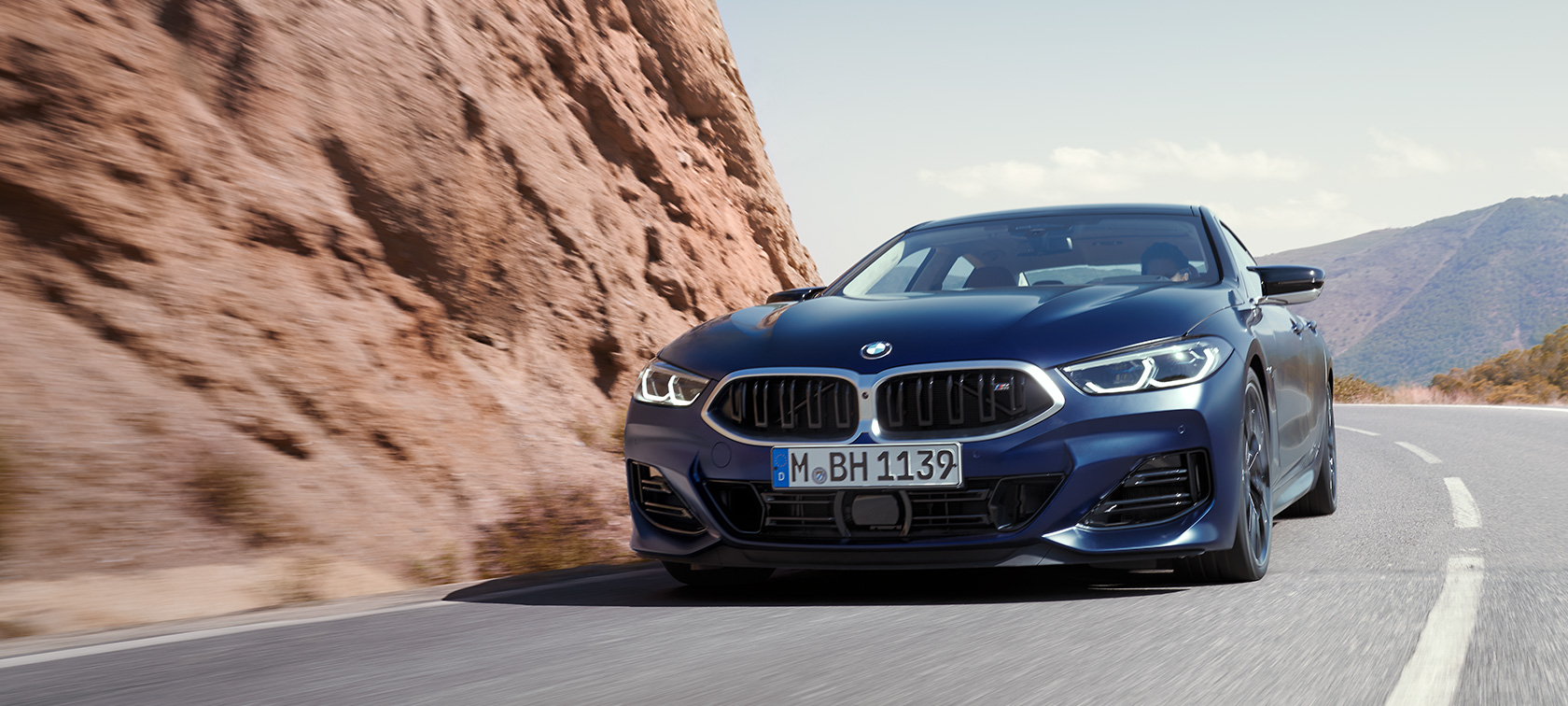 BMW 8-serie Gran Coupé G16 LCI Facelift 2022 BMW Individual Frozen Tanzanite Blue metallic set forfra let drejet kørende på en bjergvej