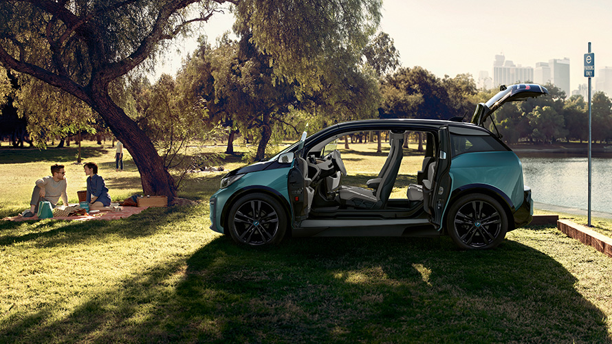 BMW i3 2018 i en park BMW i3 I01 2018 Jucaro Beige med detaljer i Frozen Grey metallic set fra siden med åbne døre i en park