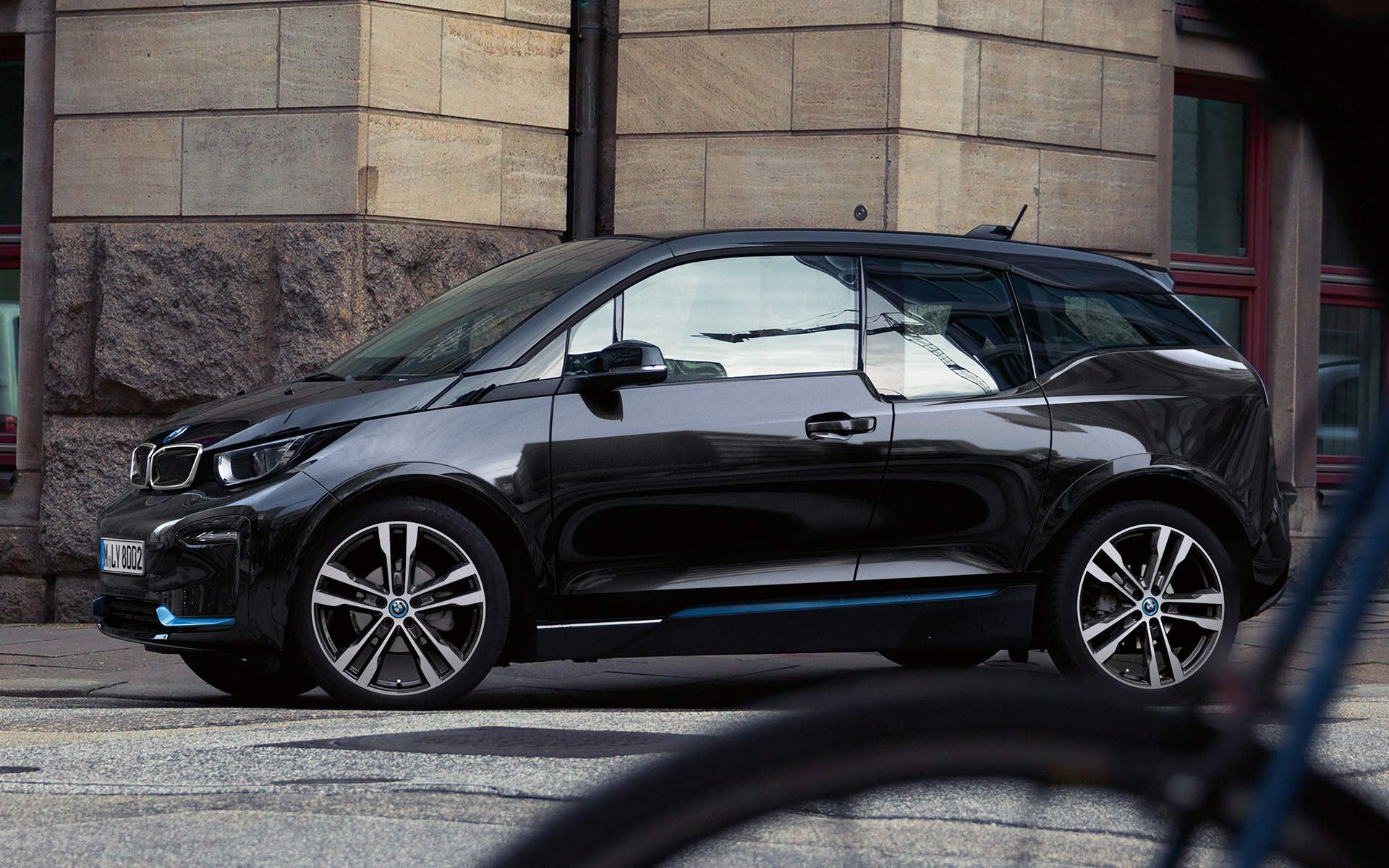 BMW i3s I01 2018 Fluid Black med detaljer i BMW i Blue set fra siden kørende i urbane omgivelser