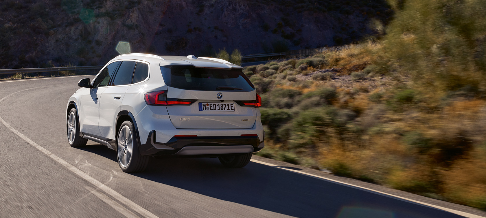 BMW iX1 U11 BEV køredynamik højdepunkt video BMW iX1 U11 BEV 2022 Mineral White metallic 2/3 visning bagfra bjergvej kørende køredynamik højdepunkt video