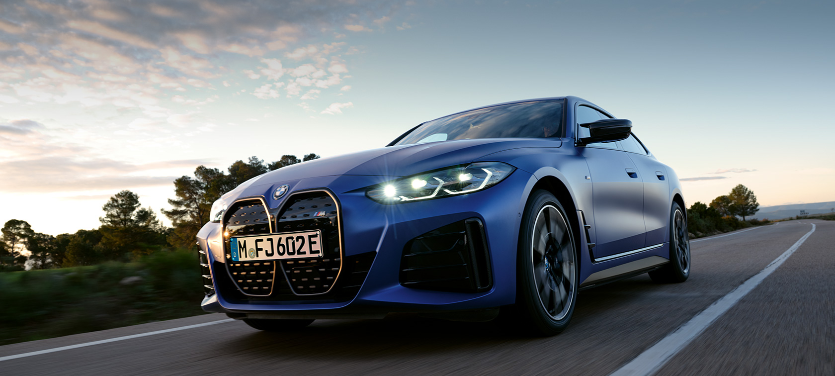 BMW i4 M50 G26 2021 set fra siden parkeret foran et stigende terræn BMW i4 M50 G26 2021 BMW Individual Frozen Portimao Blue metallic set fra siden parkeret foran et stigende terræn
