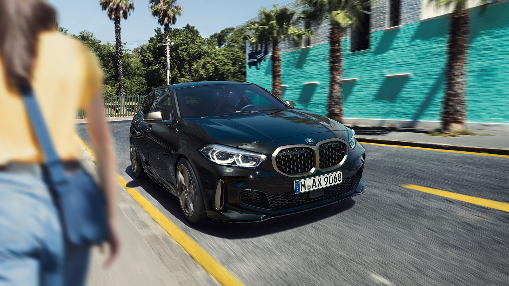 BMW M135i xDrive set forfra let drejet. BMW M135i xDrive i Sapphire Black metallic set forfra let drejet, kørende med en kvinde i forgrunden.