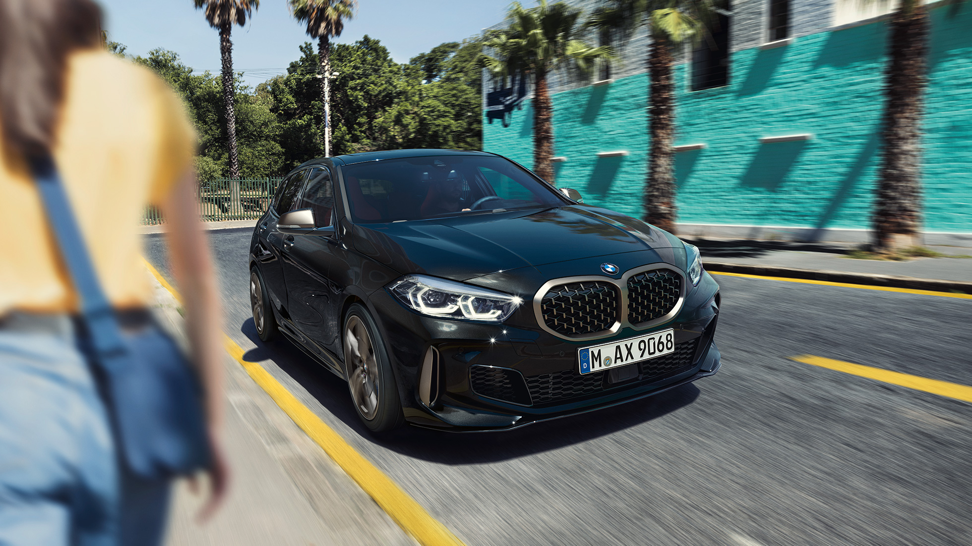 BMW M135i xDrive set forfra let drejet. BMW M135i xDrive i Sapphire Black metallic set forfra let drejet, kørende med en kvinde i forgrunden.