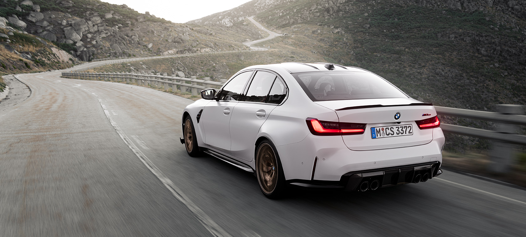 BMW M3 CS G80 set bagfra, let drejet, kørende BMW M3 G80 set bagfra let drejet kørende på en vej i bjergene