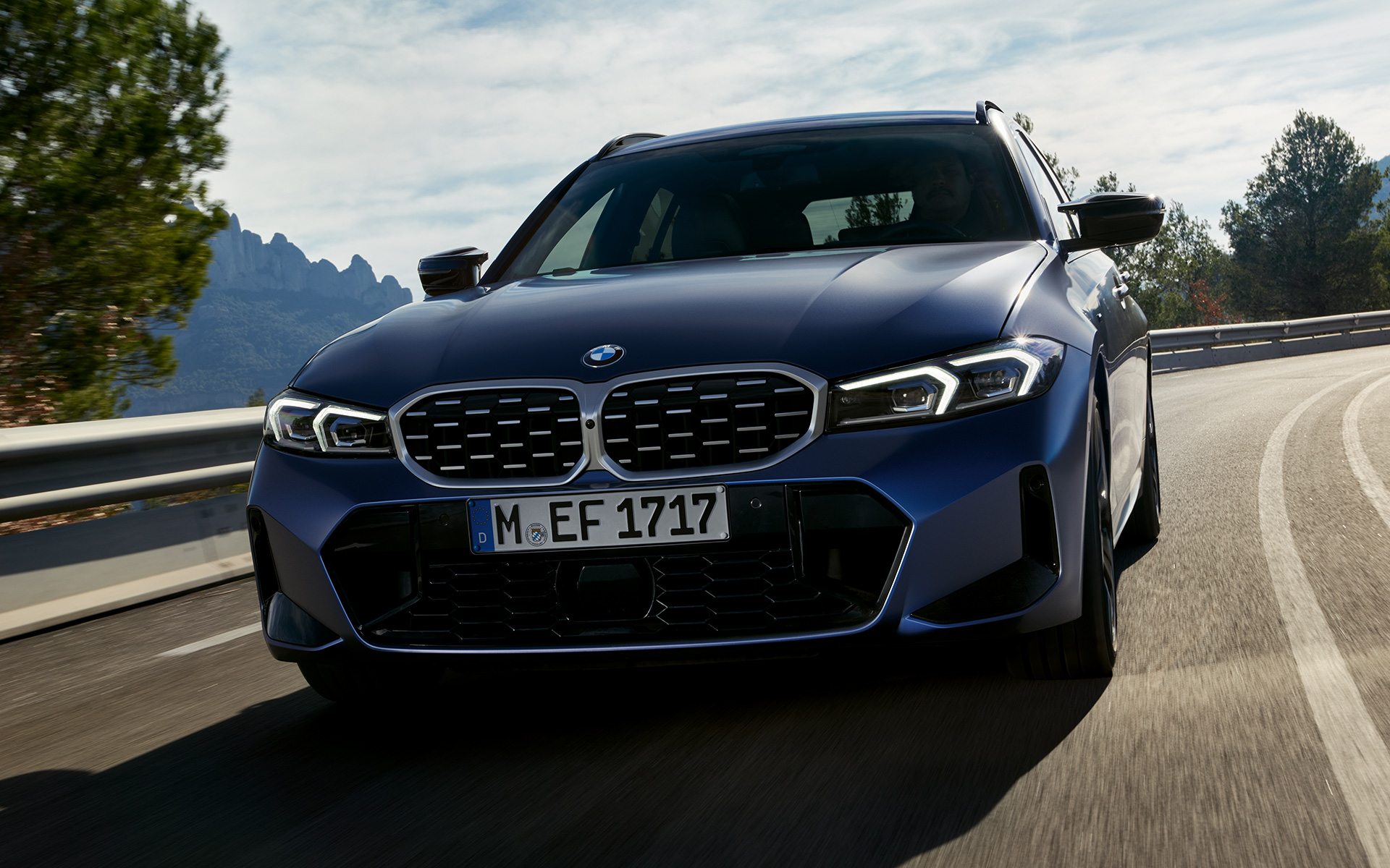 BMW M340i xDrive Touring G21, Frozen Tanzanite Blue, set forfra og kørende på en vej