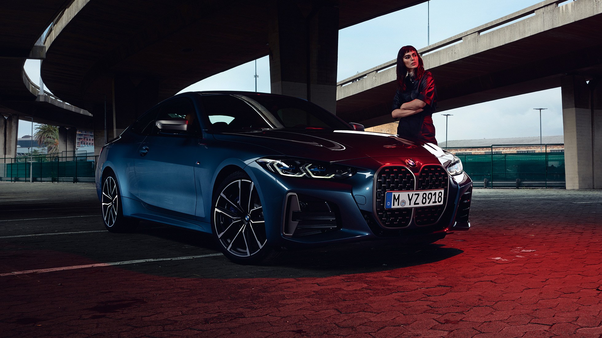 Model står ved siden af BMW M440i xDrive Coupé G22 2020 set fra siden let drejet BMW M440i xDrive Coupé Arctic Race Blue metallic G22 2020 set fra siden let drejet med model