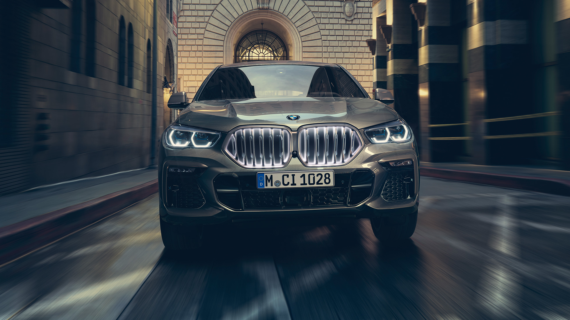 BMW X6 M50i med BMW ‚Iconic Glow‘ nyre. BMW X6 M50i set forfra foran et urbant miljø.