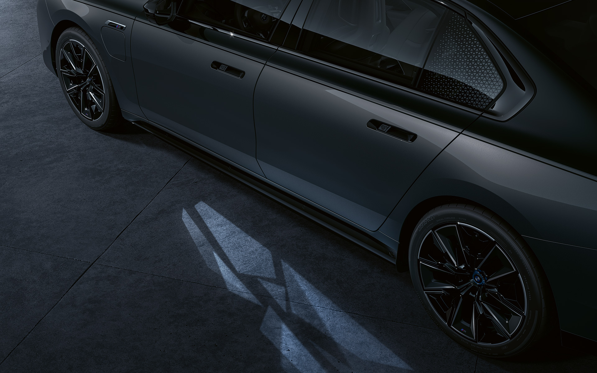 Lyskoncept BMW M760e xDrive Sedan G70 two tone-lakering Sapphire Black metallic BMW Individual Dravit Grey metallic nærbillede fra siden med tændt Welcome Light Carpet