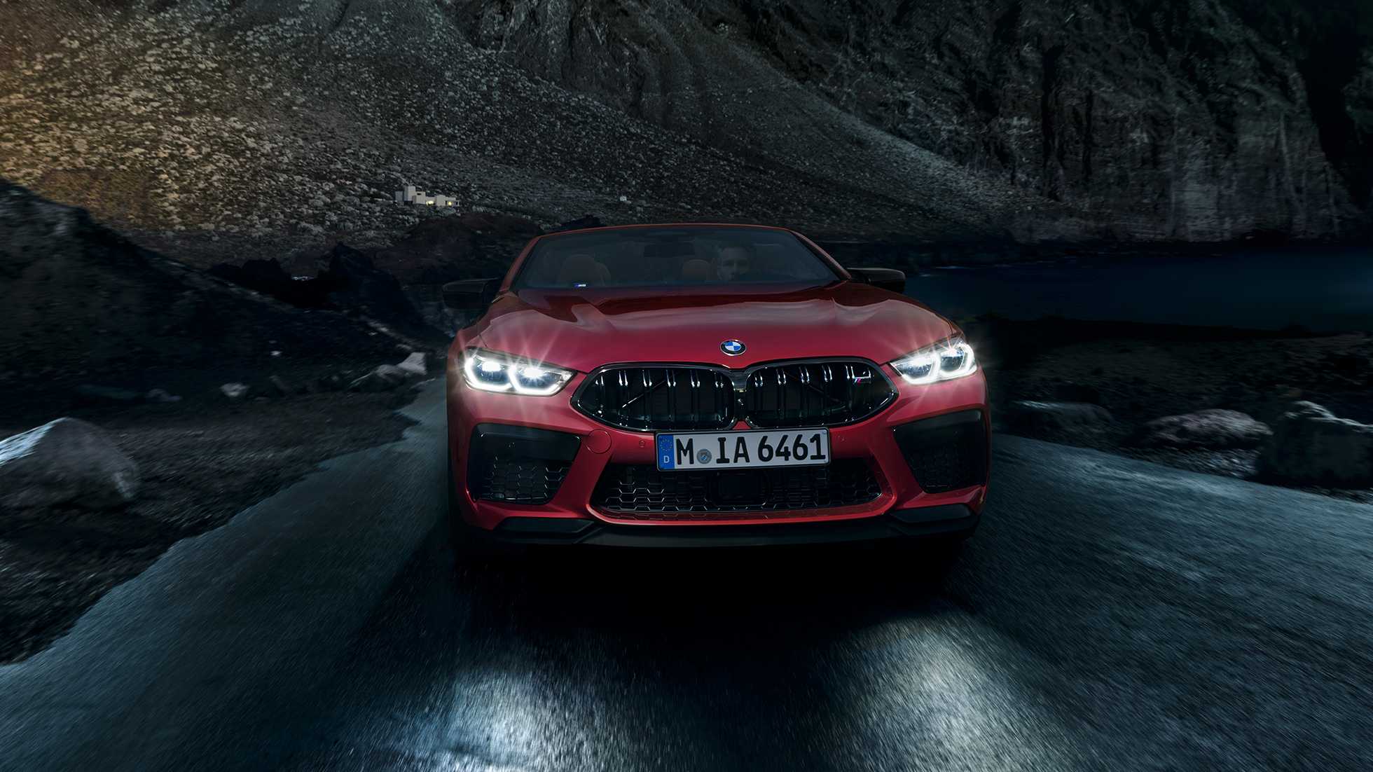 BMW M8 Competition Cabriolet set forfra. BMW M8 Competition Cabriolet i Motegi Red metallic med lysende forlygter set forfra, kørende om natten.