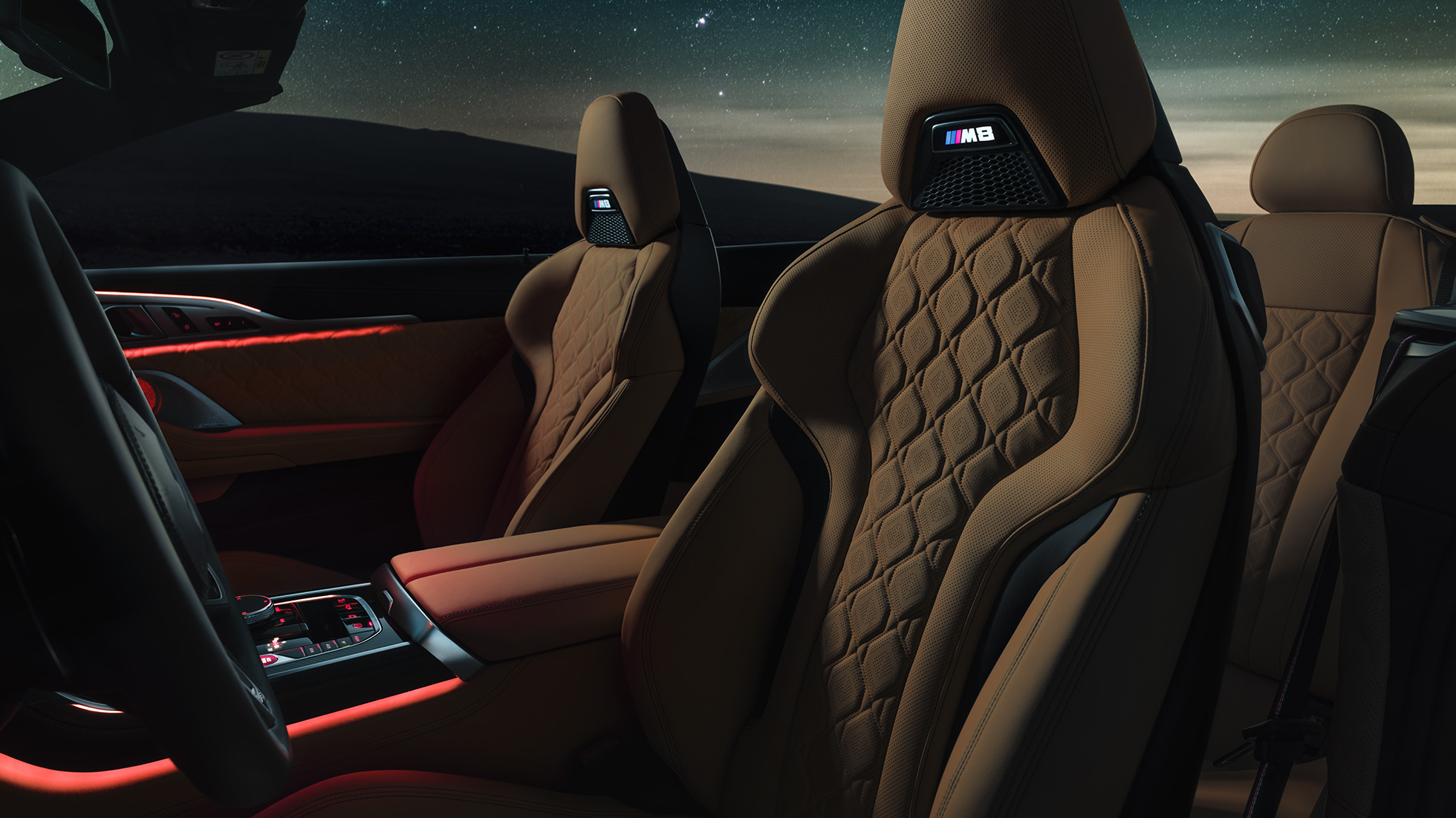 M sportssæder i 'Merino'-læder. BMW M8 Competition Cabriolet med åben kaleche under en stjernehimmel, kabine med M sportssæder i 'Merino'-læder og rødt Ambient Light.