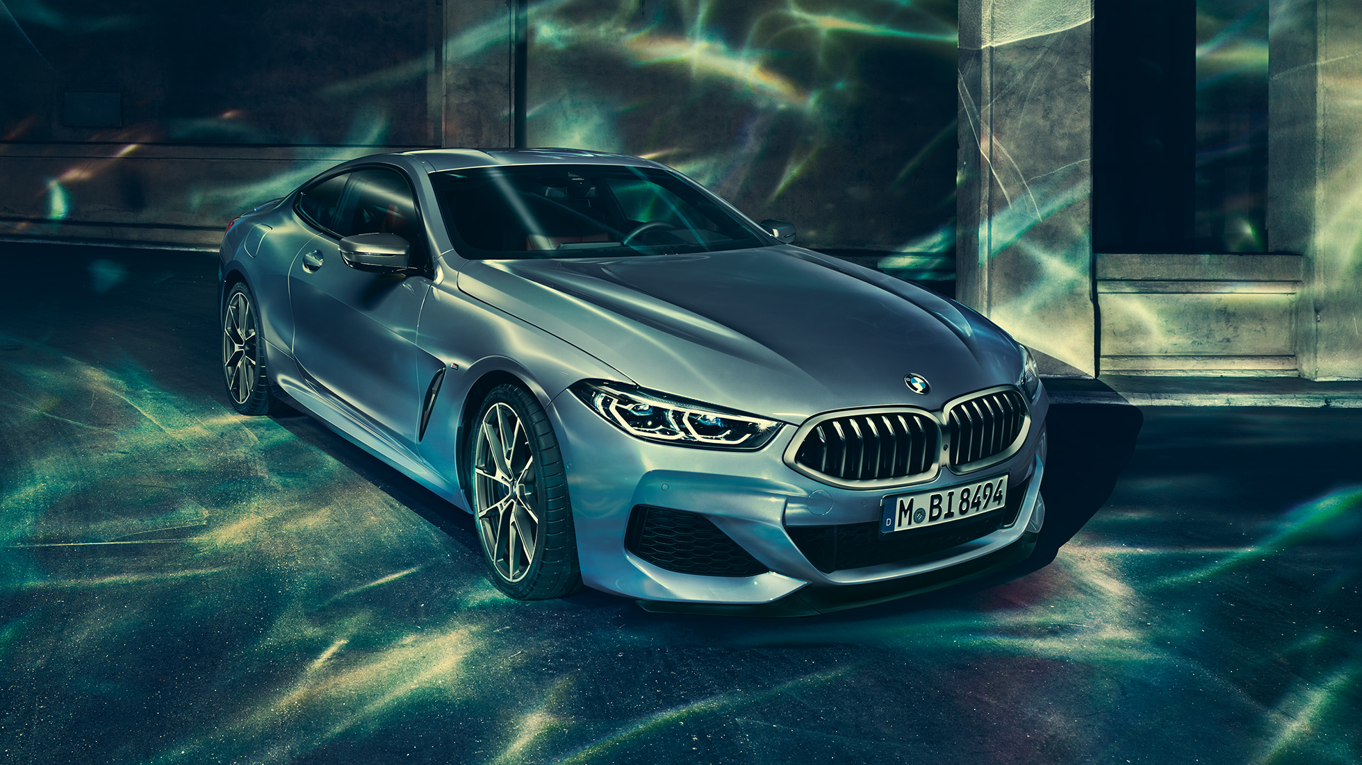 BMW M850i xDrive Coupé set forfra let drejet fra venstre. BMW M850i xDrive Coupé i Barcelona Blue metallic set forfra let drejet fra venstre, parkeret foran en bygning.