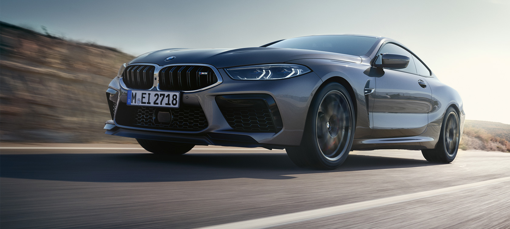 BMW M8 Coupé F92 LCI Facelift 2022 set fra siden let drejet kørende BMW M8 Coupé F92 LCI Facelift 2022 Skyscraper Grey metallic set fra siden let drejet kørende i frøperspektiv