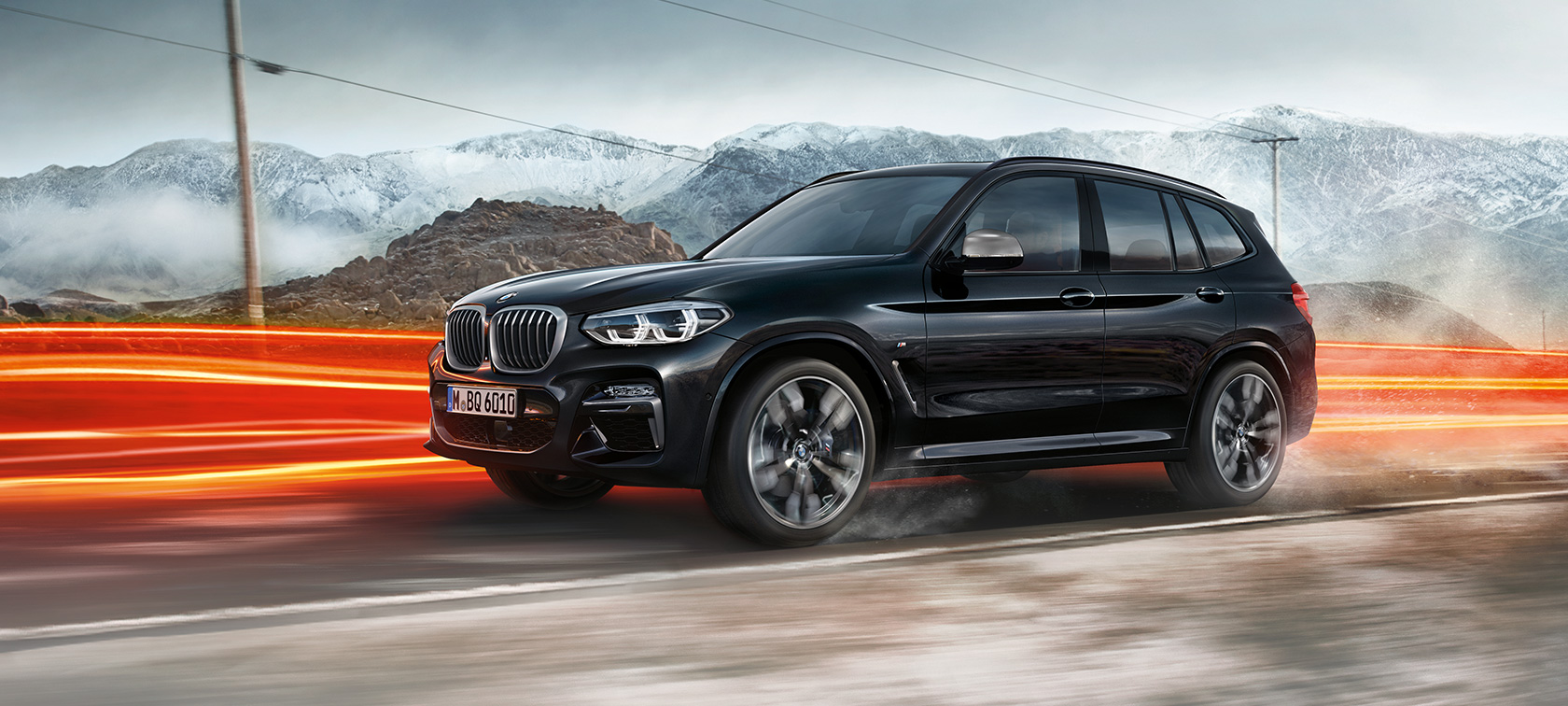 BMW X3 M40i og BMW X3 M40d, set fra siden. BMW X3 M40i i og BMW X3 M40d i safirsort metallic, kørende, eksteriør, set fra siden foran bjerglandskab med lysstriber.