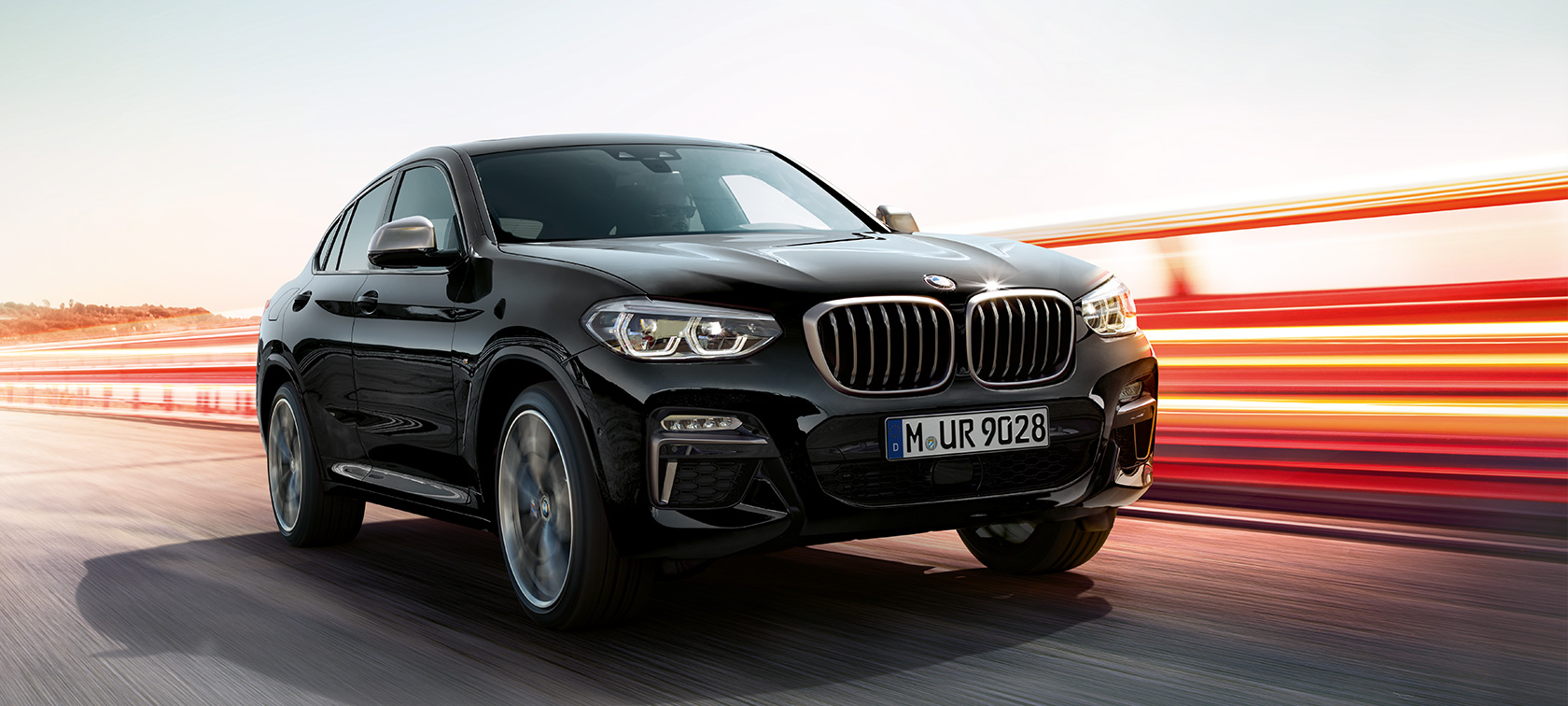 BMW X4 M40i i og BMW X4 M40d i safirsort metallic kørende, eksteriør, set forfra fra venstre, let drejet med lysstriber.