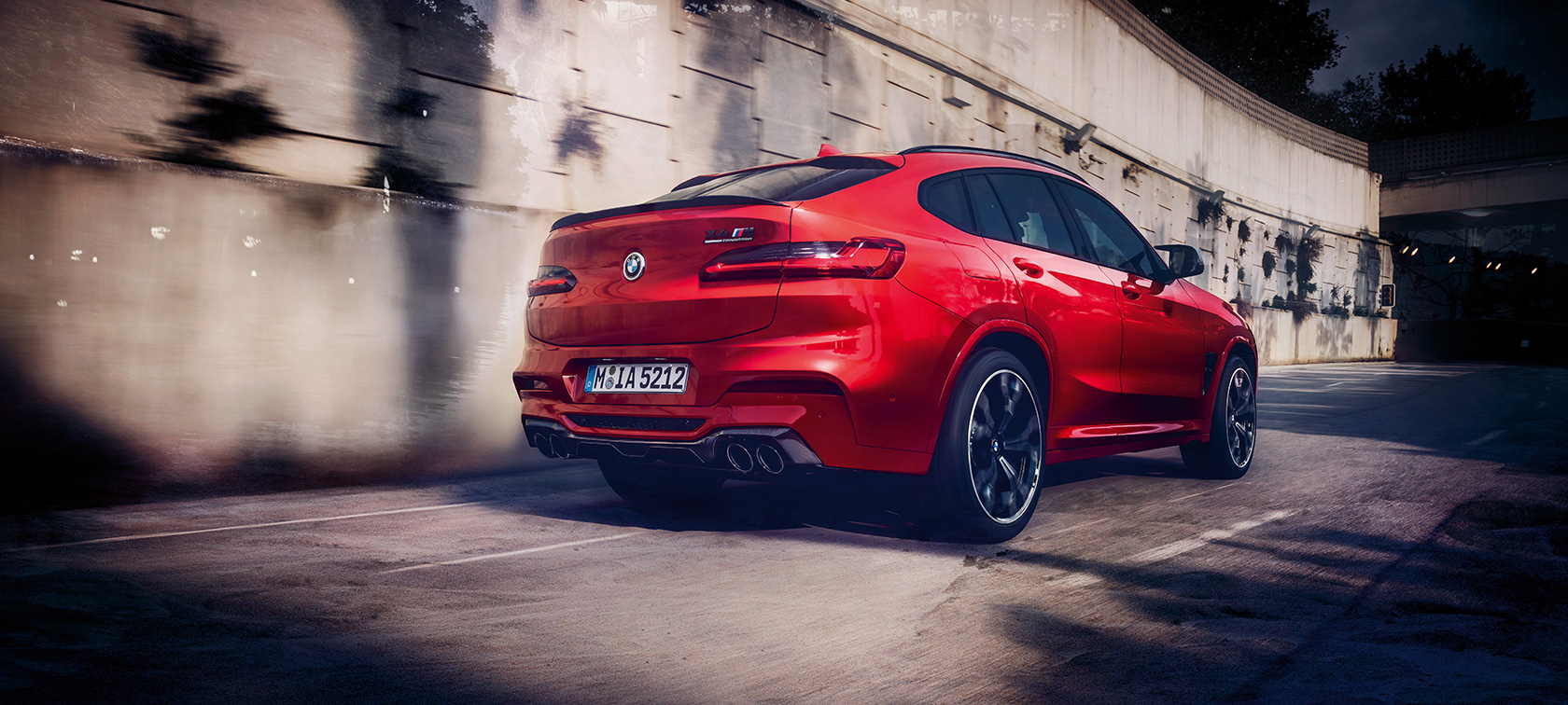 BMW X4 M Competition i Toronto rød-metallic, kørende eksteriør, set bagfra let drejet.