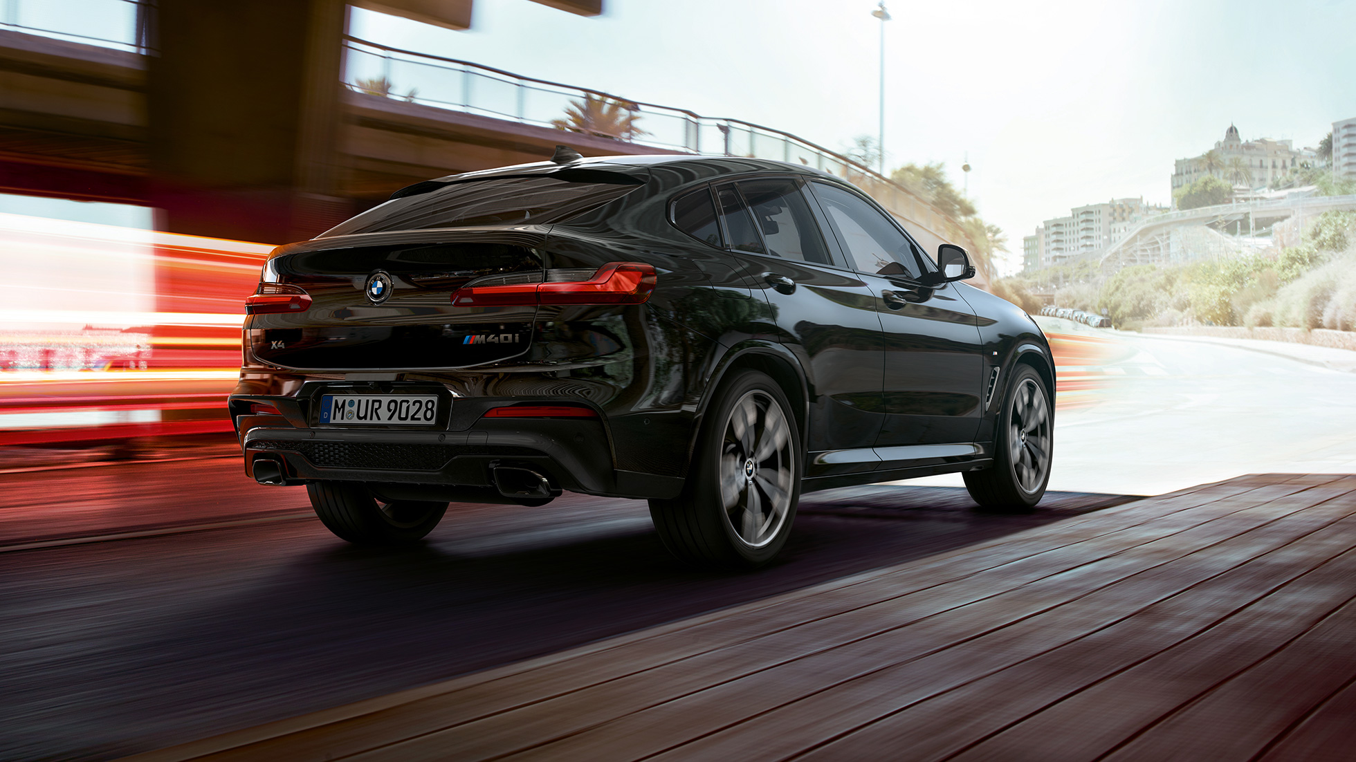 BMW X4 M40i, set bagfra let drejet. BMW X4 M40i i safirsort metallic, eksteriør, set bagfra let drejet højre med lysstriber.