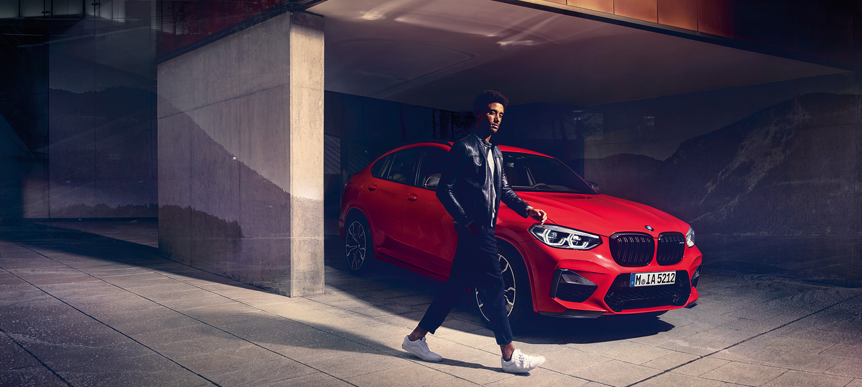 BMW X4 M Competition i Toronto rød-metallic, eksteriør, set forfra let drejet med ung mand.