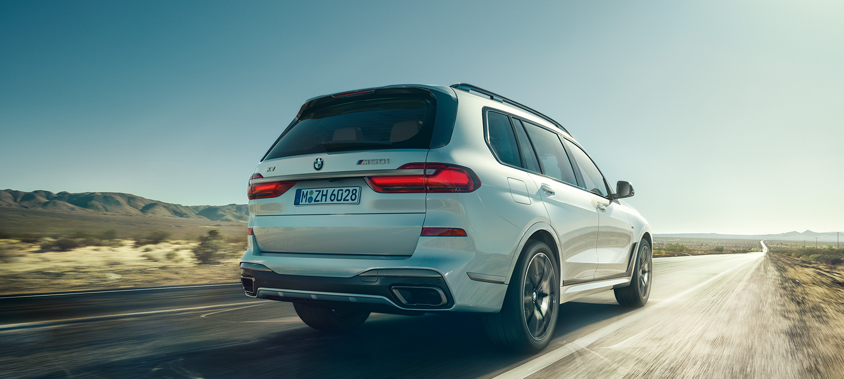 BMW X7 M50d, set bagfra BMW X7 M50d i Mineral White, kørende på en øde motorvej, set bagfra, G07, 2019