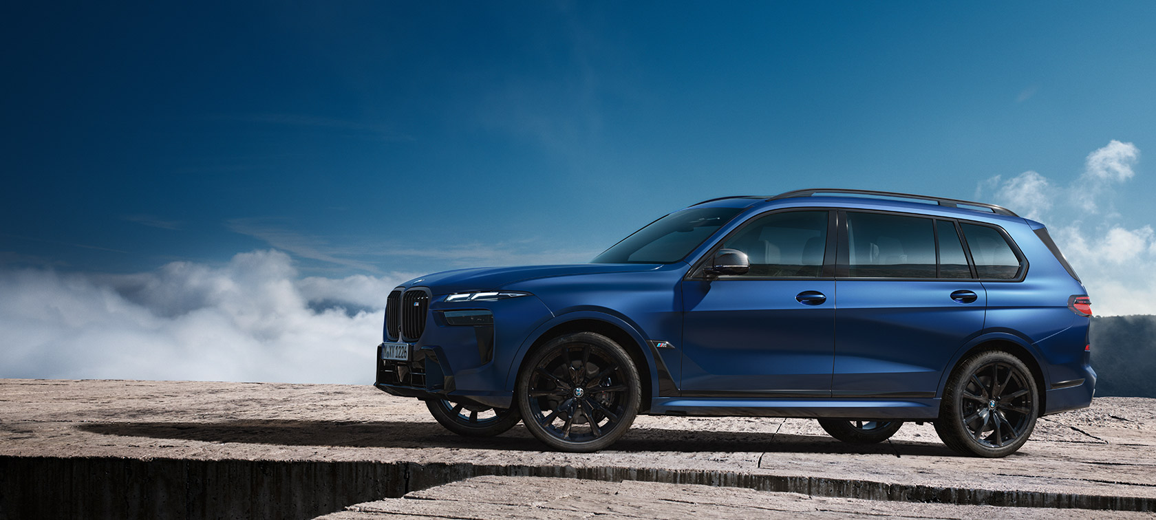 BMW X7 M60i xDrive G07 LCI Frozen Marina Bay Blue set fra siden stående foran et bjerglandskab