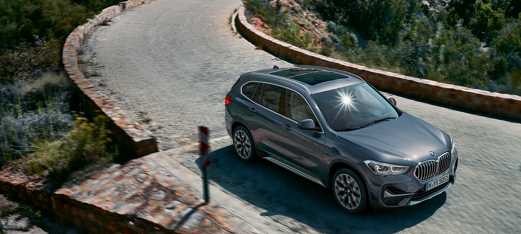 BMW X1, trekvartbillede forfra. BMW X1, trekvartbillede forfra, kørende foran en bjergkulisse.
