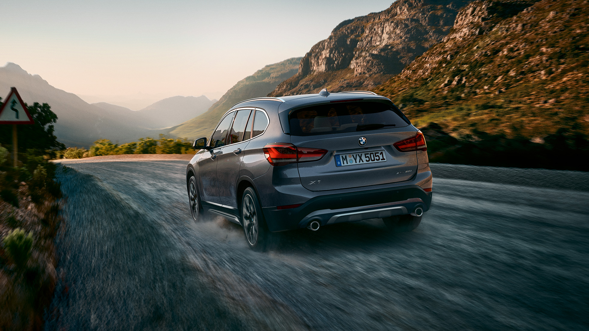 BMW X1, trekvartbillede bagfra. BMW X1, trekvartbillede bagfra, kørende foran en bjergkulisse.
