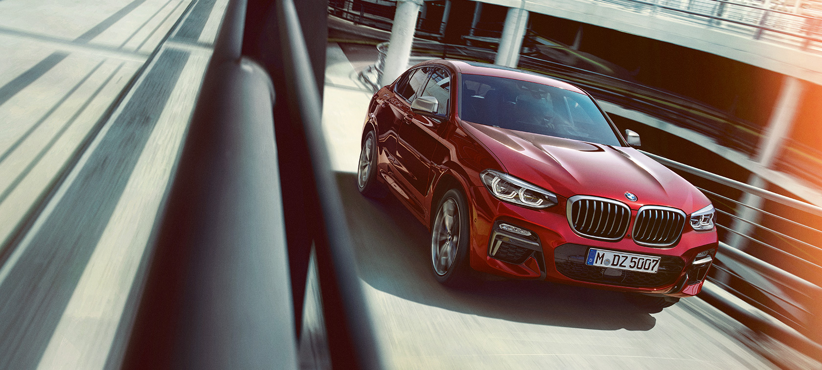BMW X4 kørende i parkeringshus BMW X4 G02 2018 Flamenco Red Brillant-effekt set fra siden let drejet kørende i parkeringshus