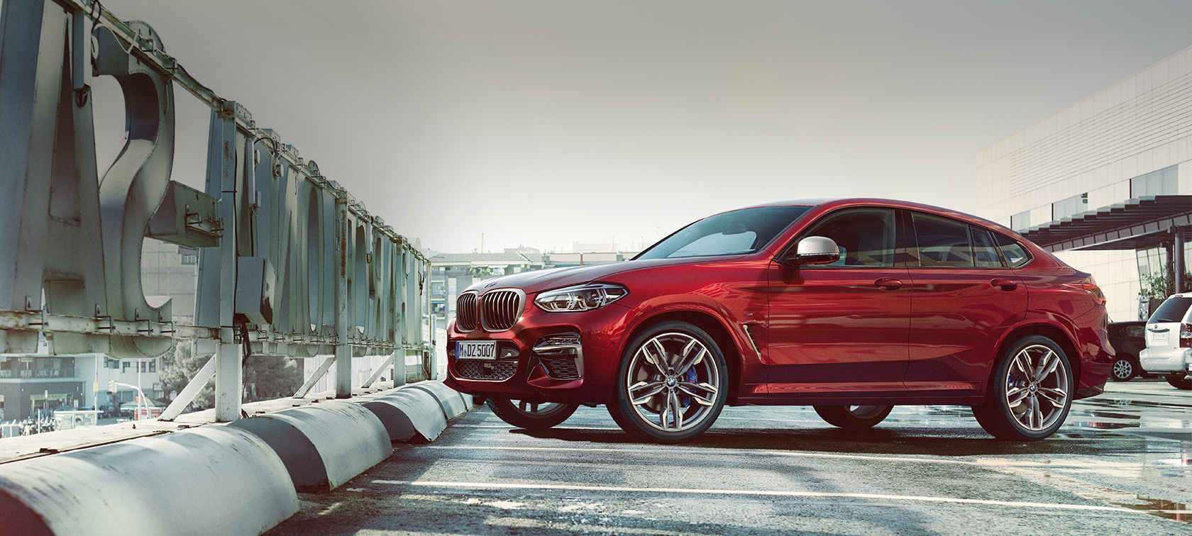 BMW X4 parkeret og set fra siden BMW X4 M40i G02 2018 Flamenco Red Brillant-effekt set fra siden parkeret på parkeringsdæk