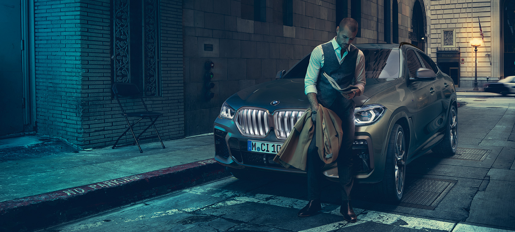 En mand læner sig op ad BMW X6. En mand læner sig op ad BMW X6 set fra siden foran et urbant miljø.