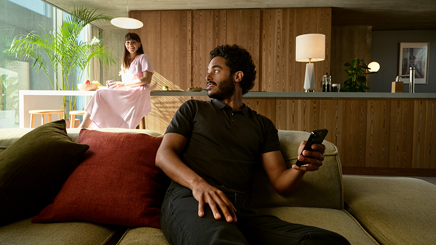 Deling BMW Digital Key BMW Digital Key deling en mand sidder med sin smartphone i hånden på en sofa med en kvinde i baggrunden
