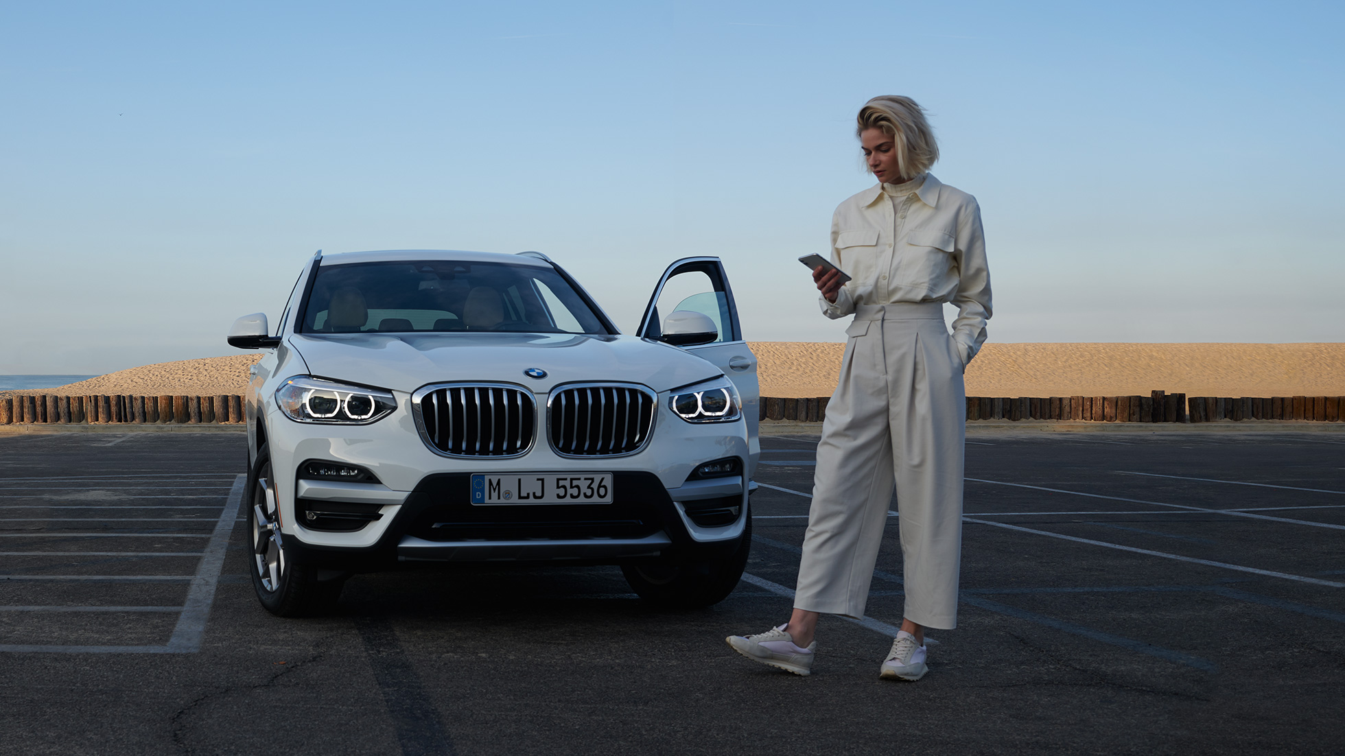 En kvinde benytter My BMW App på sin smartphone En kvinde benytter My BMW App fra BMW ConnectedDrive på sin smartphone foran en hvid BMW X5