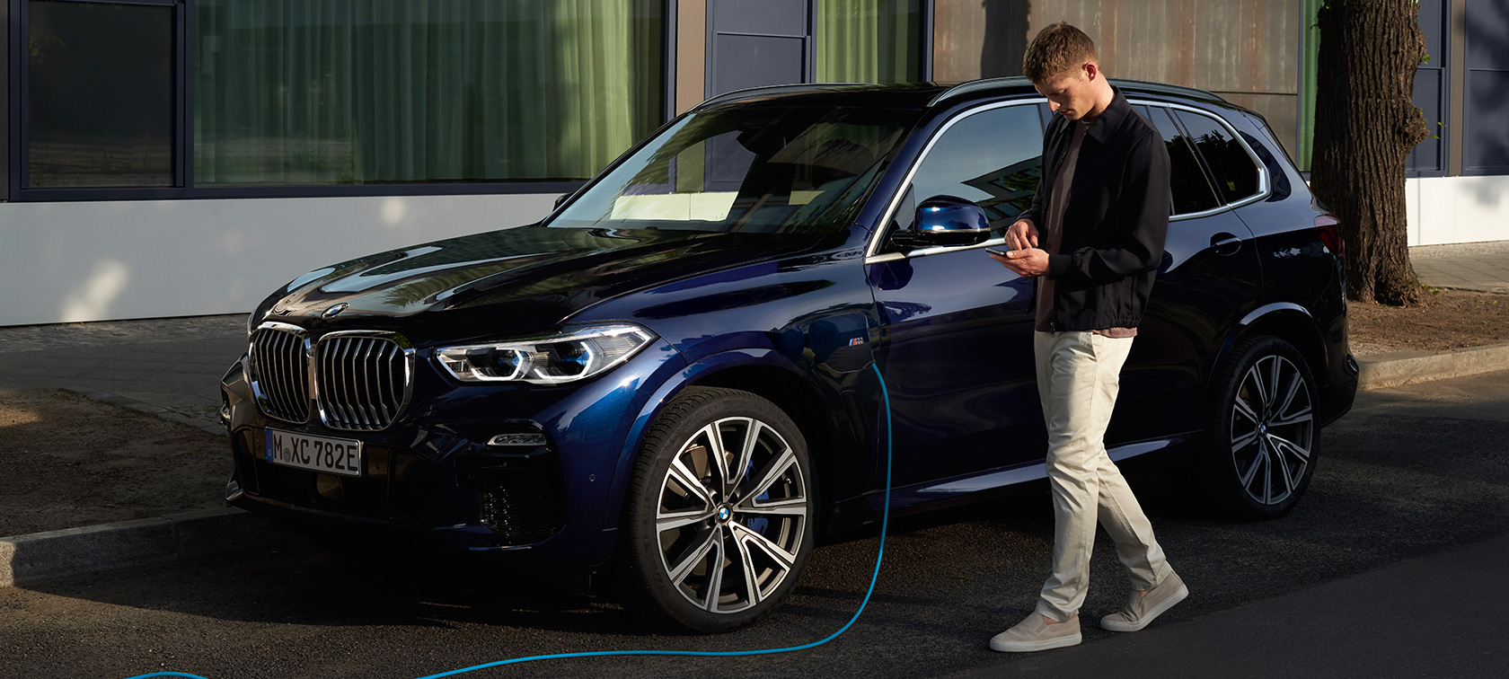 En mand benytter My BMW app på sin smartphone En mand benytter My BMW app fra BMW ConnectedDrive på sin smartphone, mens hans BMW X5 Plug-in-hybrid oplades