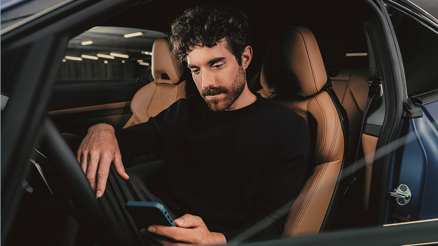 En mand sidder i en BMW En mand sidder i en BMW og kigger på sin smartphone