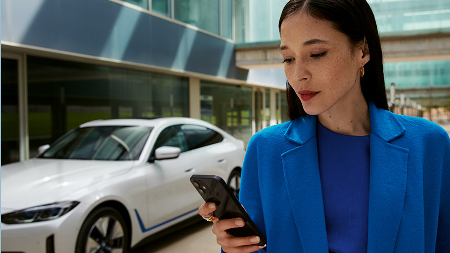 En kvinde står foran en BMW En kvinde står foran en BMW og kigger på sin smartphone