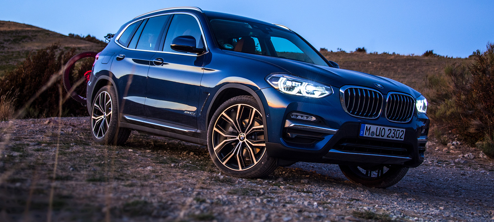 Mørkeblå BMW X3 i terræn Mørkeblå BMW X3 med cykelholder og mountainbike holder stille i terrænet