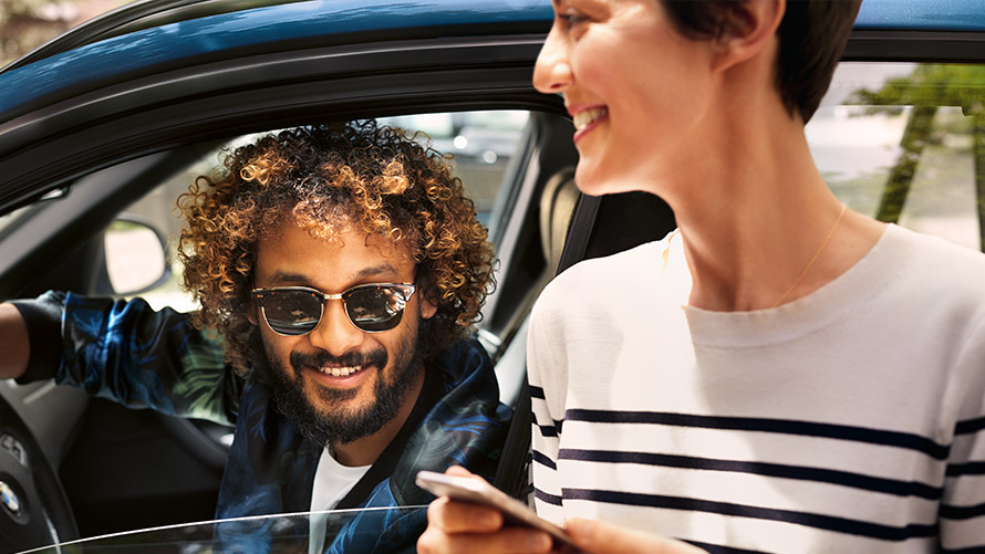 BMW Connected Mand i BMW og kvinde uden for BMW bruger BMW Connected på smartphone
